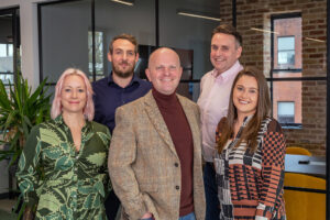 Five people standing in an office, including Hannah Parsons, Nicholas Hopkins, Matt Collingwood, Mike McEvoy and Danielle Keegan.